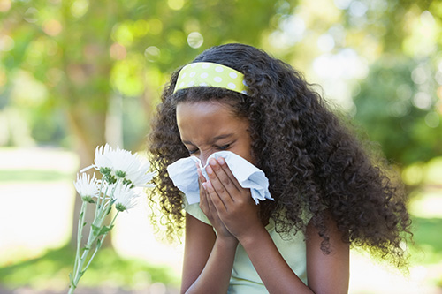 Girl sneezing outside in front of flower
