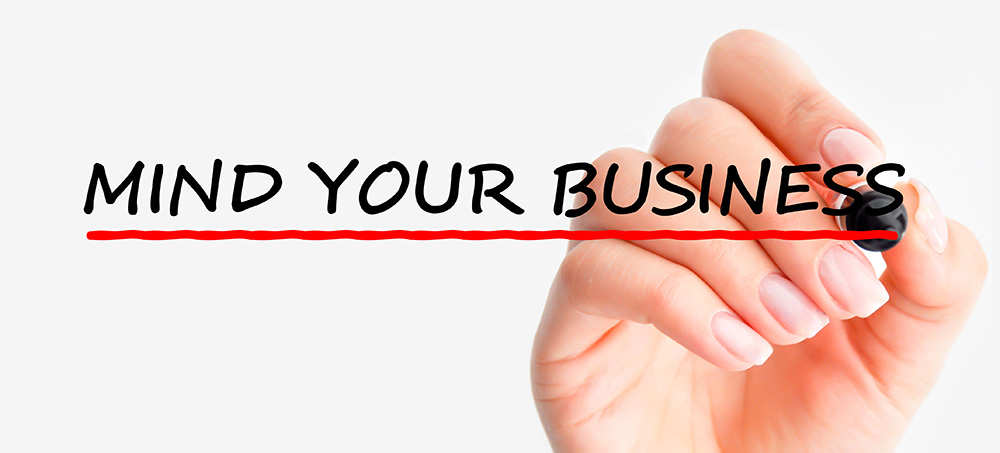 Woman's hand writing the words Mind Your Business in black marker on glass.