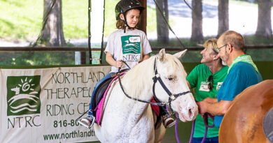 Photograph of a child riding a white horse with two trainers leading the horse at the Northland Therapeutic Riding Center in Kearney, Missouri.