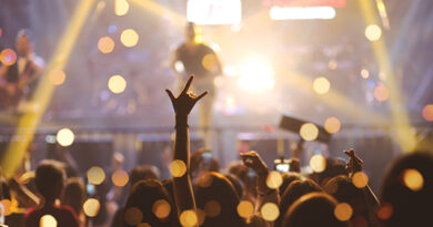 Concert goer lifts hand in crowd during concert with musicians on stage.