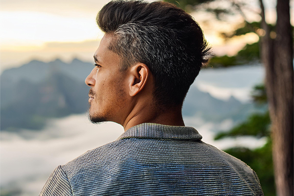 AI image of man staring into the distance with a mountain range and tree in background.