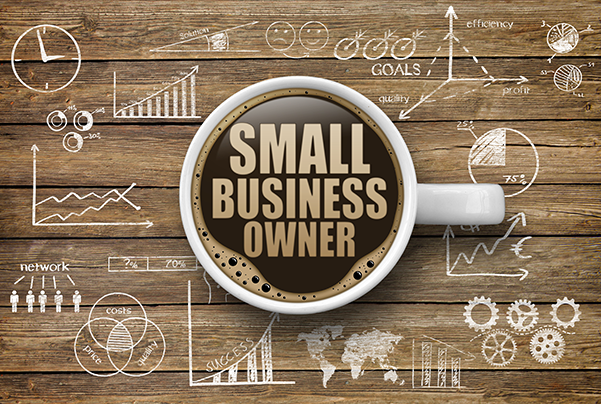 Cup with Small Business Owner written in coffee and charts surrounding it on a table.