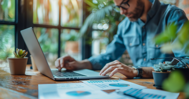 Man working on business paperwork and laptop at desk surrounded with plants.