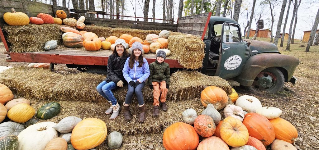 Family sitting in front of Fun Farm Truck surrounded by pumpkins.