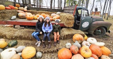 Family sitting in front of Fun Farm Truck surrounded by pumpkins.
